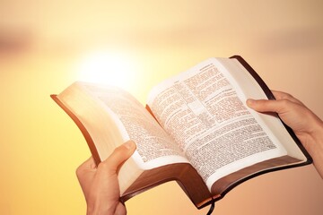 Hand holding bible book up to the sky. Religious belief, faith and worship concept.