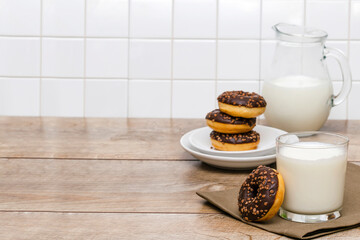 Obraz na płótnie Canvas Mini donuts covered with chocolate glaze served with bottle, jug, glass of milk. Stack of tasty sweet sugar creamy or icing doughnuts dessert food on plate and napkin on kitchen. national donuts day
