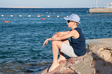 teen boy sitting on rocks by the sea