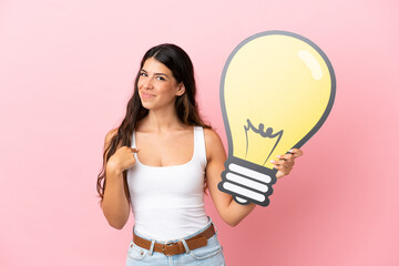 Young caucasian woman isolated on pink background holding a bulb icon and pointing it