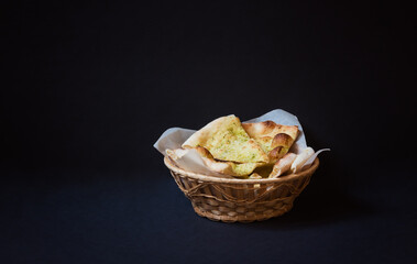 Wheat focaccia bread with aromatic pesto sauce in wicker basket on dark background.