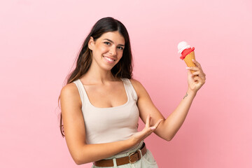 Young caucasian woman with a cornet ice cream isolated on pink background extending hands to the side for inviting to come