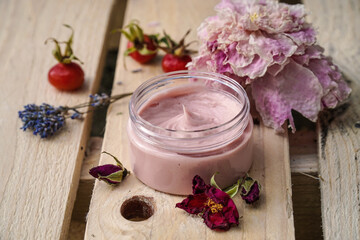 Obraz na płótnie Canvas Homemade pink face or body cream wit lavender and wild rose flowers and rosehips on the wooden background. 