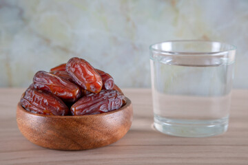 Glass of water with a bowl of date fruit on a wooden background.Muslims break the fast with water and dates