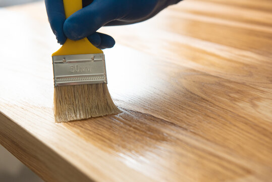 A man covers an oak table with oil with a yellow brush in blue rubber gloves. oiled wooden table top.
