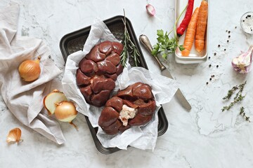 Raw beef kidneys ready to cook with vegetables and herbs on marble kitchen table. Flat layot, copy...