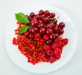 Assorted red fresh berries on a plate on a white background.