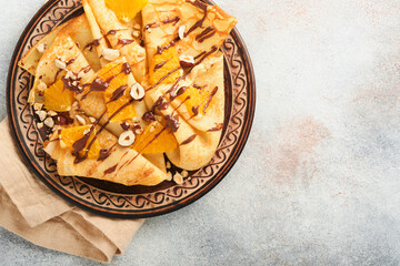Crepes suzette with oranges and chocolate. Thin crepes with chocolate spread, hazelnuts and orange slices fruit in plate for breakfast on old concrete rustic table background. Copy space. Top view