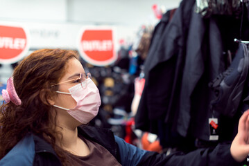 Real, young woman with protective mask shopping for clothes in an outlet store.