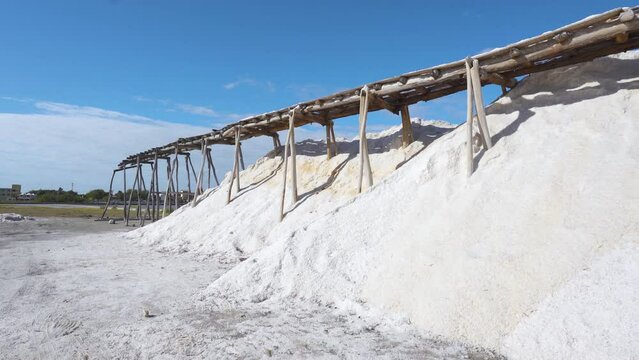 Mountains of sea salt on a tropical peninsula in the Dominican Republic. Extraction of table salt by garden method. Wooden supports under the railroad yf against the sky.