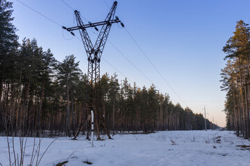 Winter landscape of power lines in a snowy field near the forest