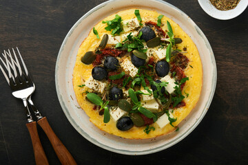 Scrambled eggs. Light, Fluffy and Buttery Scrambled Eggs with feta cheese, sun-dried tomatoes and black olives on plate over old dark wooden rustic background. Delicious breakfast. Top view, flat lay.
