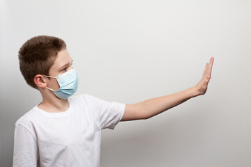 Caucasian boy in the medical mask and white T-shirt putting his hand forward and stopping something