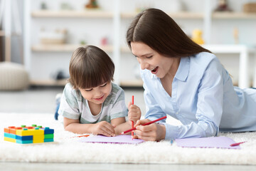 Creative development. Cute happy little boy drawing colorful picture with pencils, studying with young cheerful mother