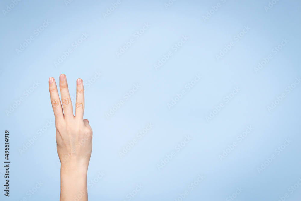 Wall mural Female hand shows number three. Woman hand showing three fingers, pointing fingers up on light blue background