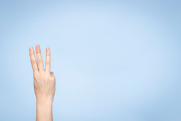 Female hand shows number three. Woman hand showing three fingers, pointing fingers up on light blue...