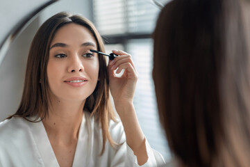 Beautiful Millennial Lady Doing Daily Makeup Near Mirror In Bathroom, Applying Mascara