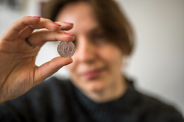 Silver 10 Ukrainian Hryvnia Coin with Cyrillic Alphabet Letters held in the Hand of a Woman Looking at it From the Background - obrazy, fototapety, plakaty
