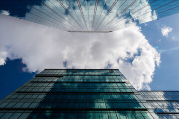 Widok na biznesowe drapacze chmur z dolnej perspektywie patrzac w niebo. Widoczne odbicia szkla w barwach niebieskich oraz zielonych