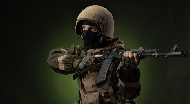 a Russian soldier in a helmet in military clothes with a Kalashnikov assault rifle on a dark background in the studio