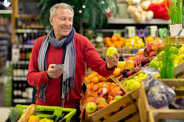 Smiling man using cell phone while shopping at supermarket