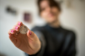 Economic Concept of Silver Color Ukrainian Hryvnia Coin in Woman's Hand with Pink Painted Nails with Defocused Background of Her in Her Room
