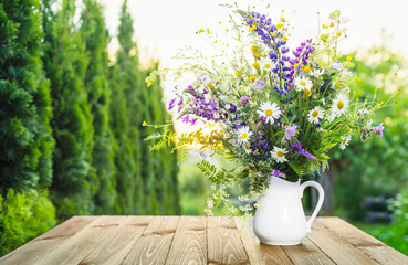 Beautiful meadow summer flowers in a vase on a sunny wooden patio. chamomiles bouquet in sunset sunlight. Copy space. Romantic picnic or weekend