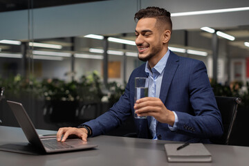 Healthy arabic businessman drinking water while working on laptop
