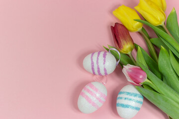 Fototapeta na wymiar Easter border composition with Easter eggs and yellow and red tulips on a pink background. A stylish concept of minimalist decor. Space for copying. Festive flat banner with greeting card