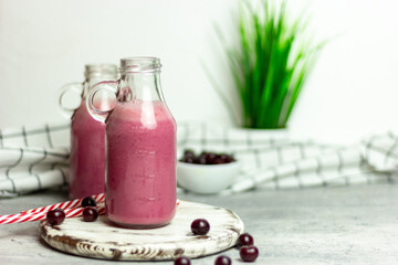 A bottle of cherry smoothies on a white background, cherries in bulk and in a plate. Morning summer breakfast
