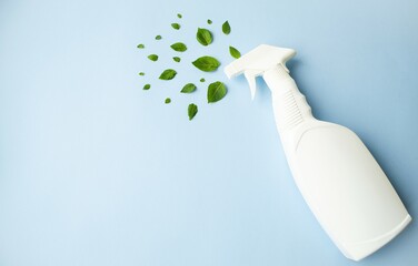 On a blue background, a white plastic bottle with cleaning agent and fresh green leaves.  Concept eco products for cleaning.  Flat lay.  Creative composition.  Space for copy text.