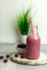 A bottle of cherry smoothies on a white background, cherries in bulk and in a plate. Morning summer breakfast