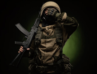 a soldier in military clothes and helmet, with a Kalashnikov rifle covers his face with his hand...