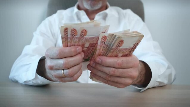 Close-up of an unrecognizable businessman counting cash of five thousand Russian ruble banknotes sitting at a table. A male cashier counts banknotes.