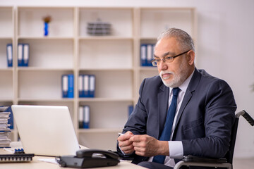 Old male employee in wheel-chair sitting at workplace