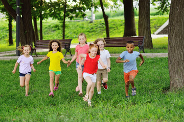 group of children of boys and girls of different races are running on the green grass against the background of a recreation park. Children's Day,