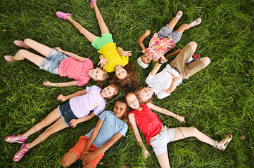 children of different races and nationalities lie on the grass in colorful clothes and smile.