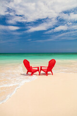 Fototapeta na wymiar Ocean waves on sandy beach with red chairs