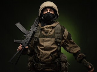 a Russian soldier in a helmet in military clothes with a Kalashnikov assault rifle on a dark...