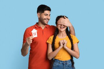 Fototapeta premium Loving Arab Man Holding Paper House Figure And Surprising His Excited Girlfriend