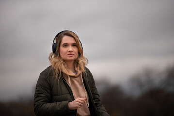 young woman listening to music with headphones on a cloudy day - 495524795