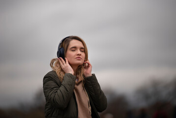 young woman listening to music with headphones on a cloudy day - 495524798