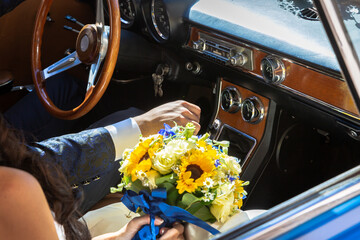 Groom driving a vintage sport car with a beautiful bridal bouquet next to him. Internal view of the car.