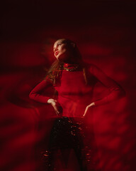 Fashion portrait with move effect and art lighting. Confident woman wearing red turtleneck, sequin trousers, posing in darkness