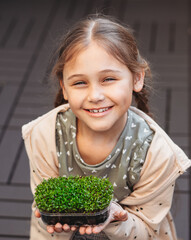 The child is happy with the sprouts of fresh greens. The little girl holds in her hands a green piece of the plantation