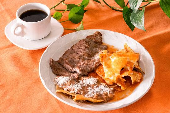 Plato de chilaquiles con frijoles y arrachera, junto a taza de caf&eacute; 