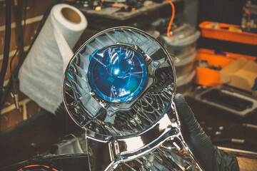 Car headlight in repair close-up. An auto mechanic wearing gloves installs the lens into the...