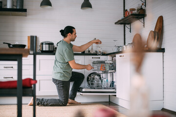 Weekend homework. A young man takes out clean dishes from the dishwasher in the kitchen at home.