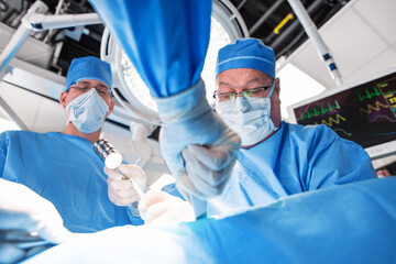 Male Caucasian doctors wearing scrubs performing patient surgery