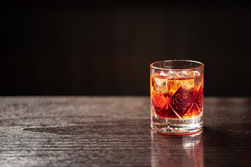Crystal glass of classic negroni cocktail with ice on dark background